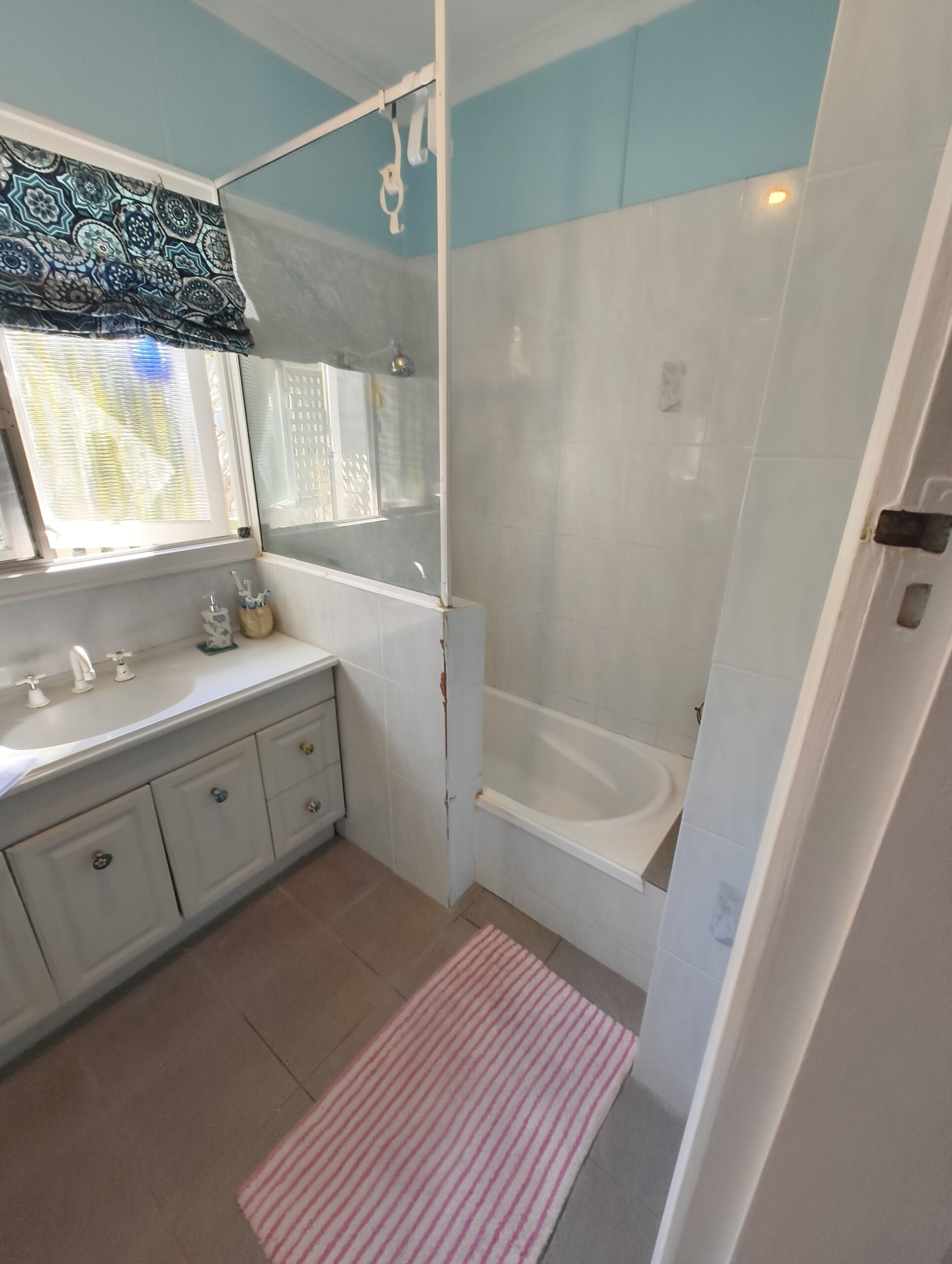 Graceville Queenslander bathroom before renovation with built-in bath and dated pale blue tiles