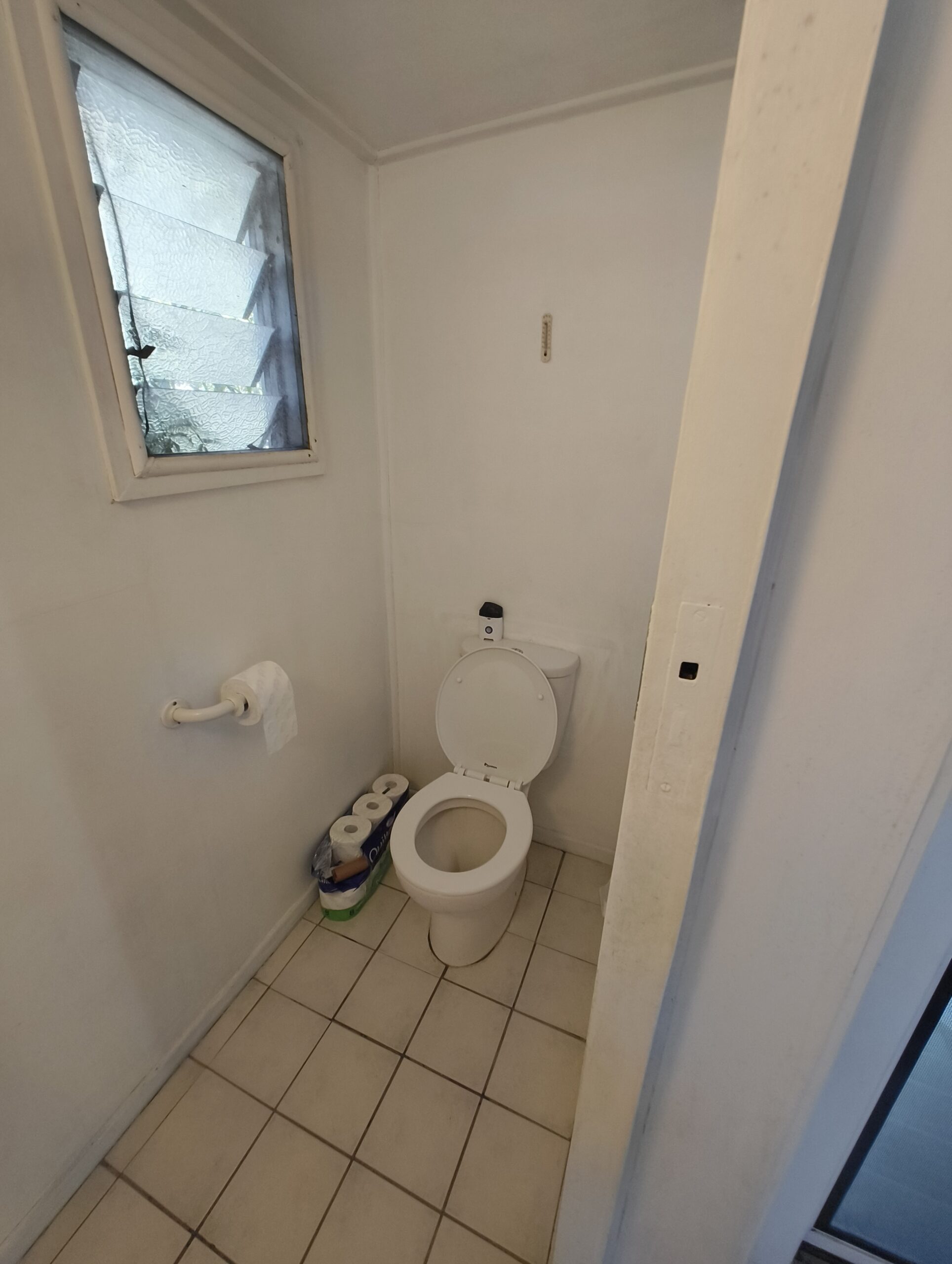 Separate toilet before renovation in a Graceville Queenslander with original window and dated tiles