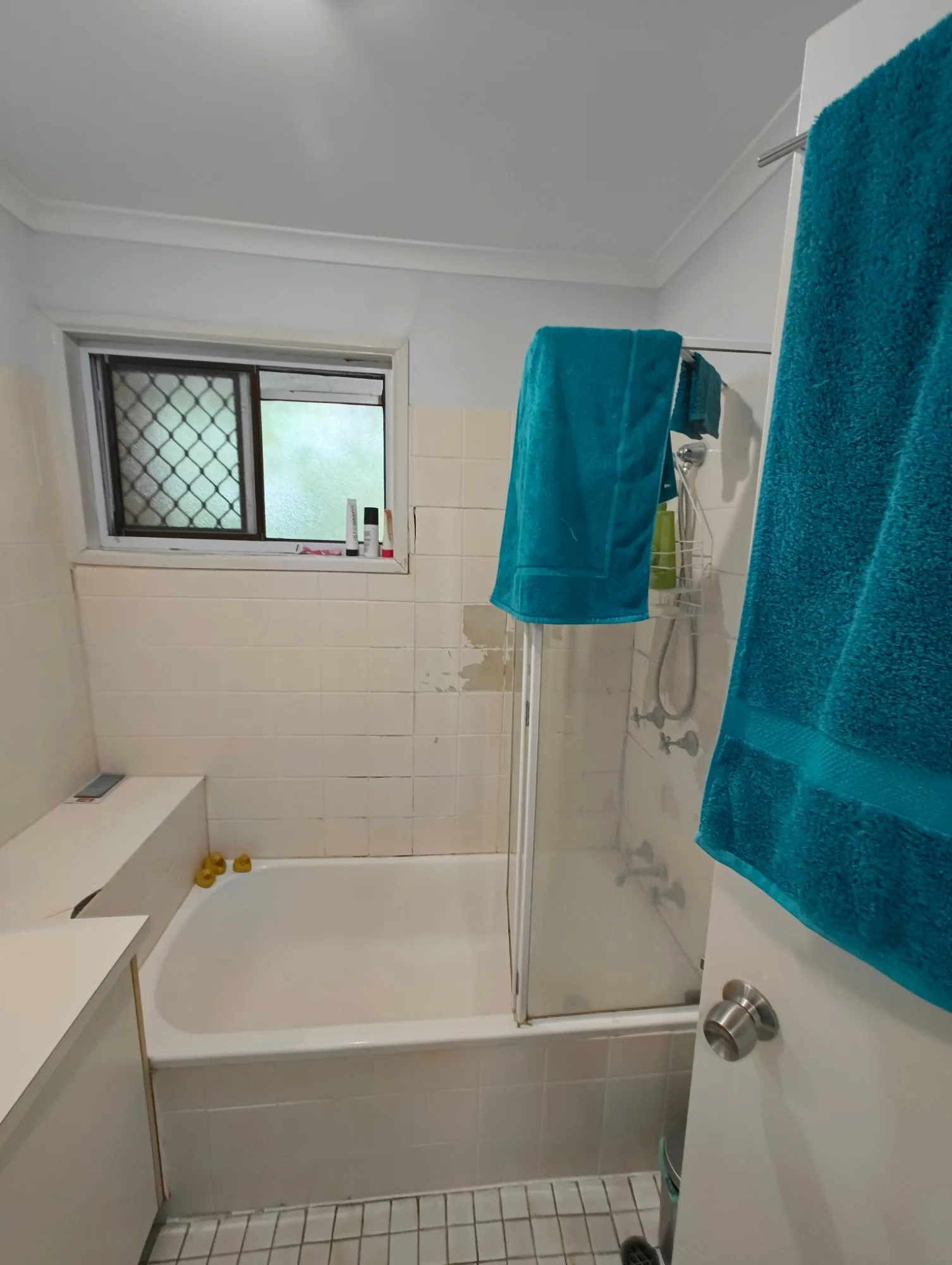 Bath with shower screen and peeling tiles in the Red Hill bathroom before renovation